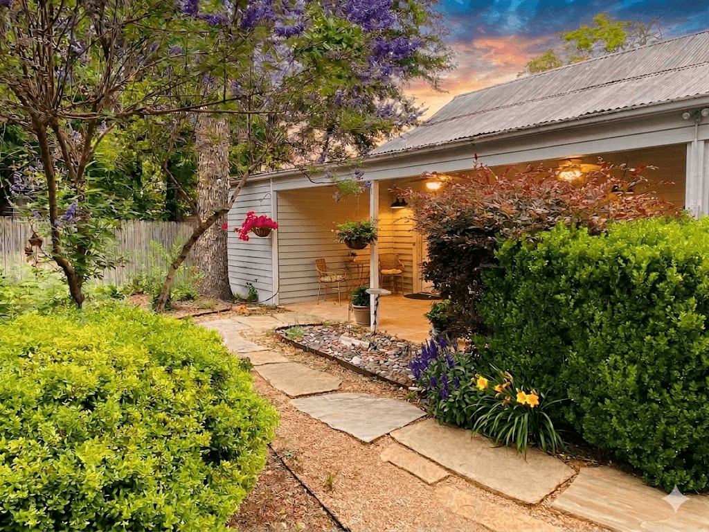 Flagstone pathway through lush garden leading to Juniper cottage patio at golden hour with purple jacaranda tree